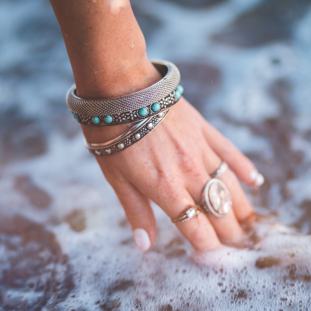 Woman hand near the ocean waves wearing bohemian bracelets and rings